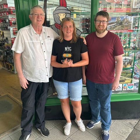 Paul, Lindsey and Mark Boyland, the family that runs Chester Model Centre, stood in front of the shop on Chester Rows looking at the camera smiling while Lindsay holds the trophy for SME News UK Enterprise Awards Best Model Train Store of the year Cheshire