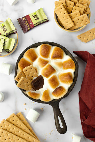 black-skillet-of-marshmallows-with-smores-ingredients-on-white-table