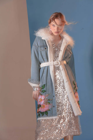 Una modelo muestra una chaqueta de denim con forro de peluche y bordados de flores rosadas.