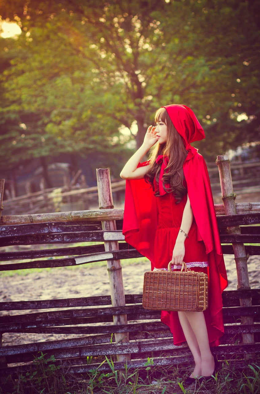 A girl dressed as Little Red Riding Hood stands near a wooden fence