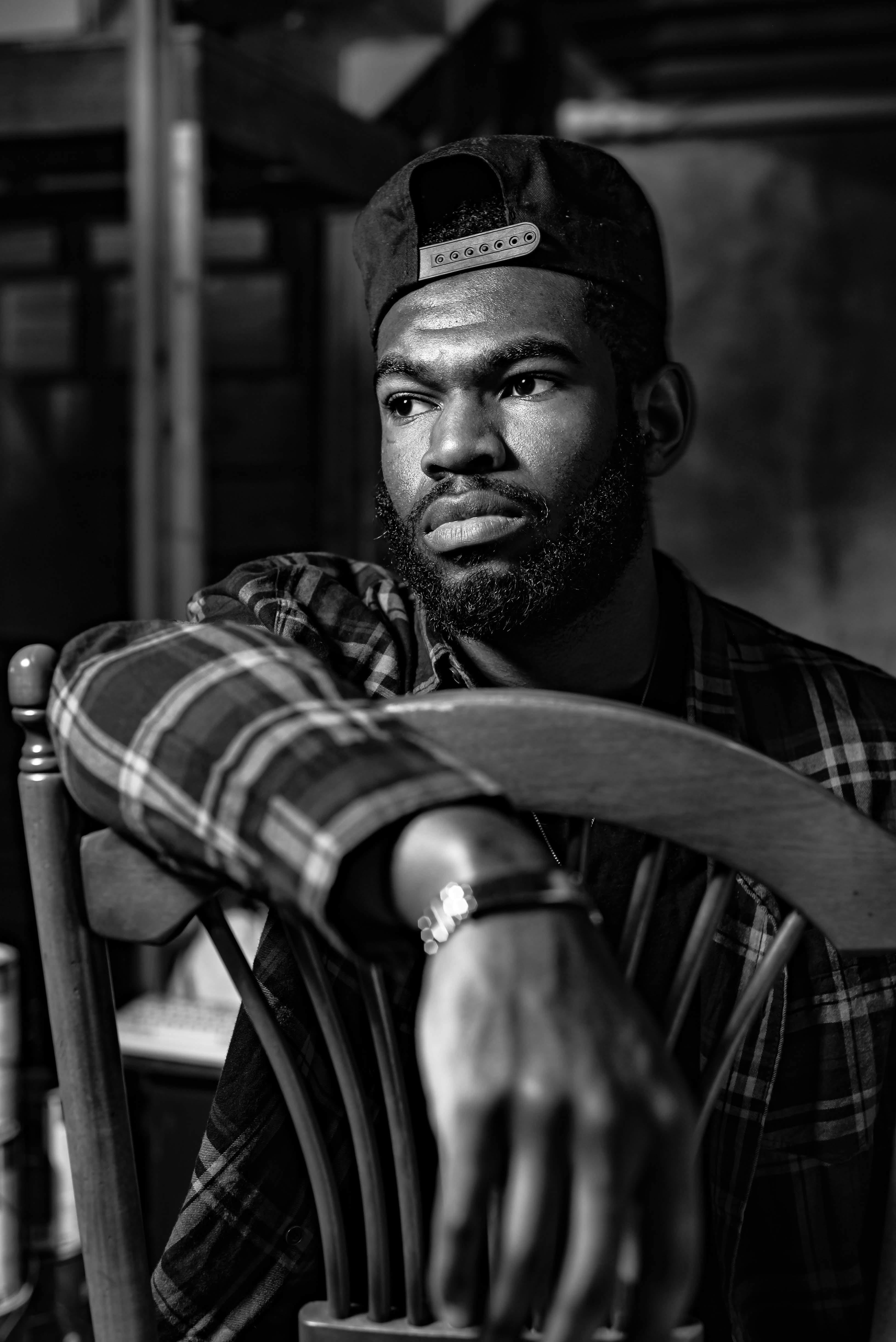 A man in a plaid shirt and baseball cap sits on a chair