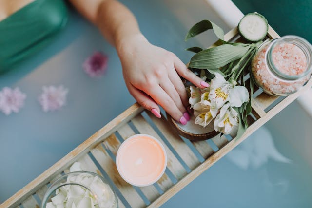 Woman lying in the bathtub, flowers and spa products on a wooden tray on the bathtub