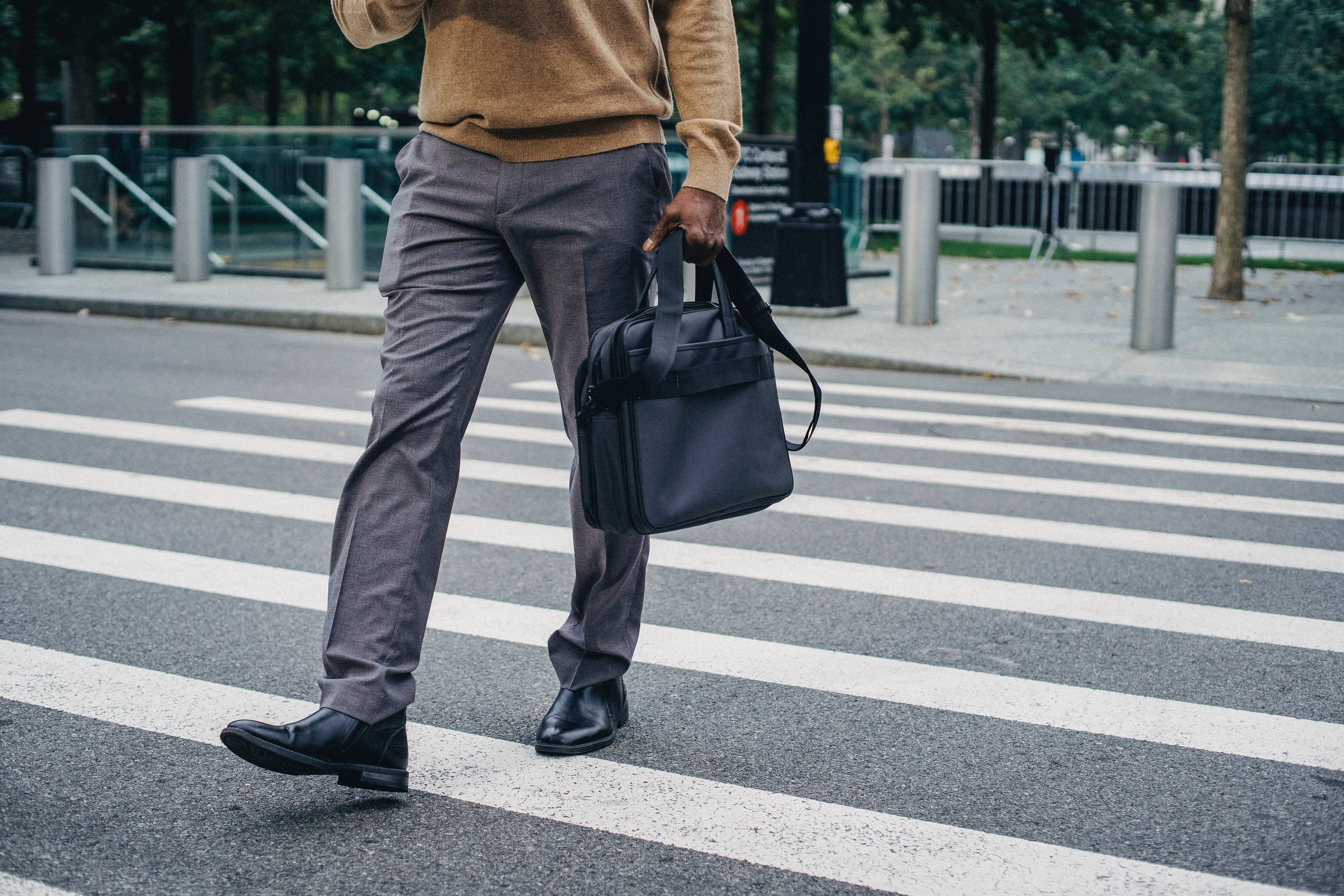  A man in gray trousers with a bag in his hand crosses the road