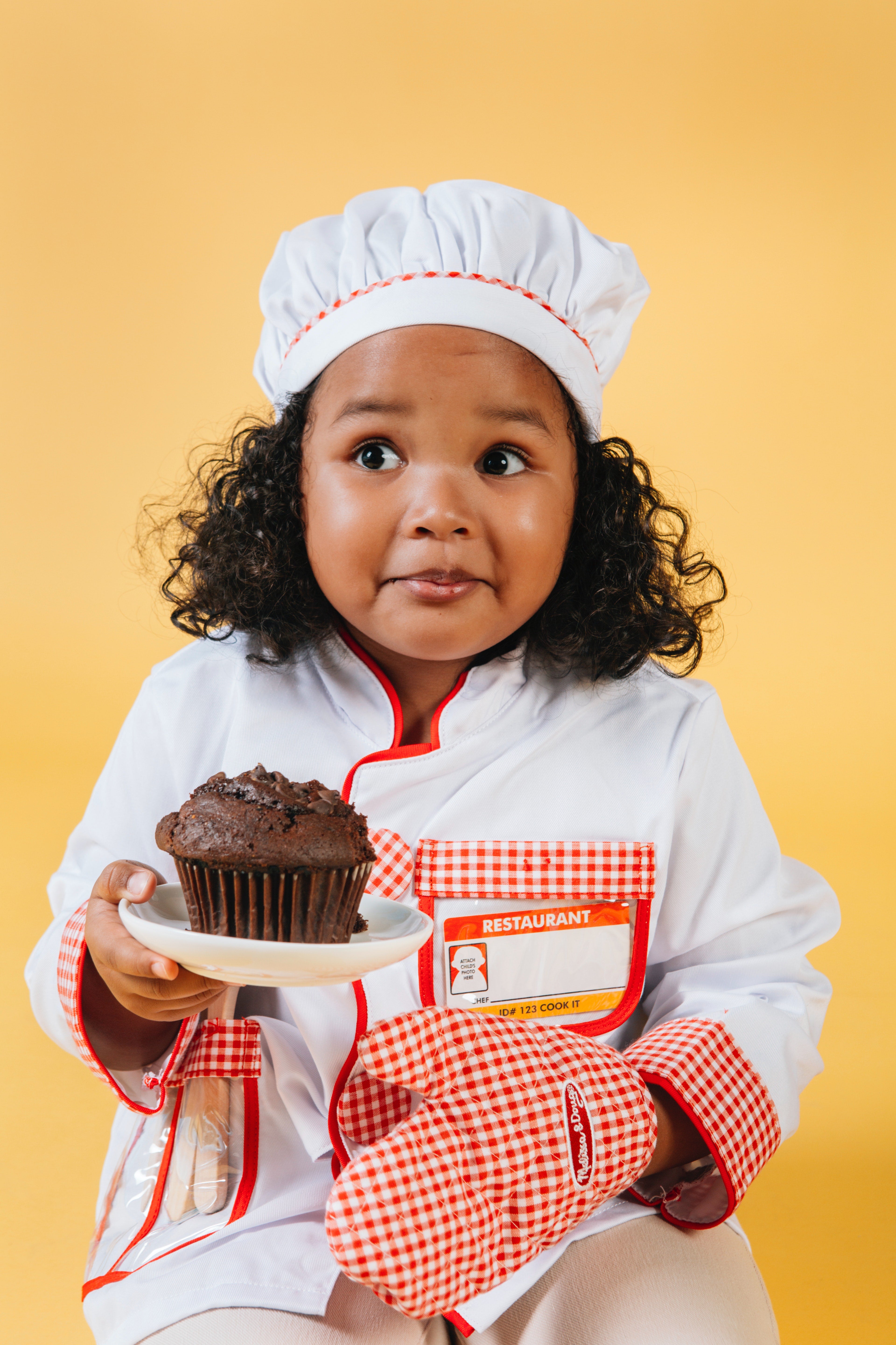 A girl in a chef's costume holds a plate with a cupcake