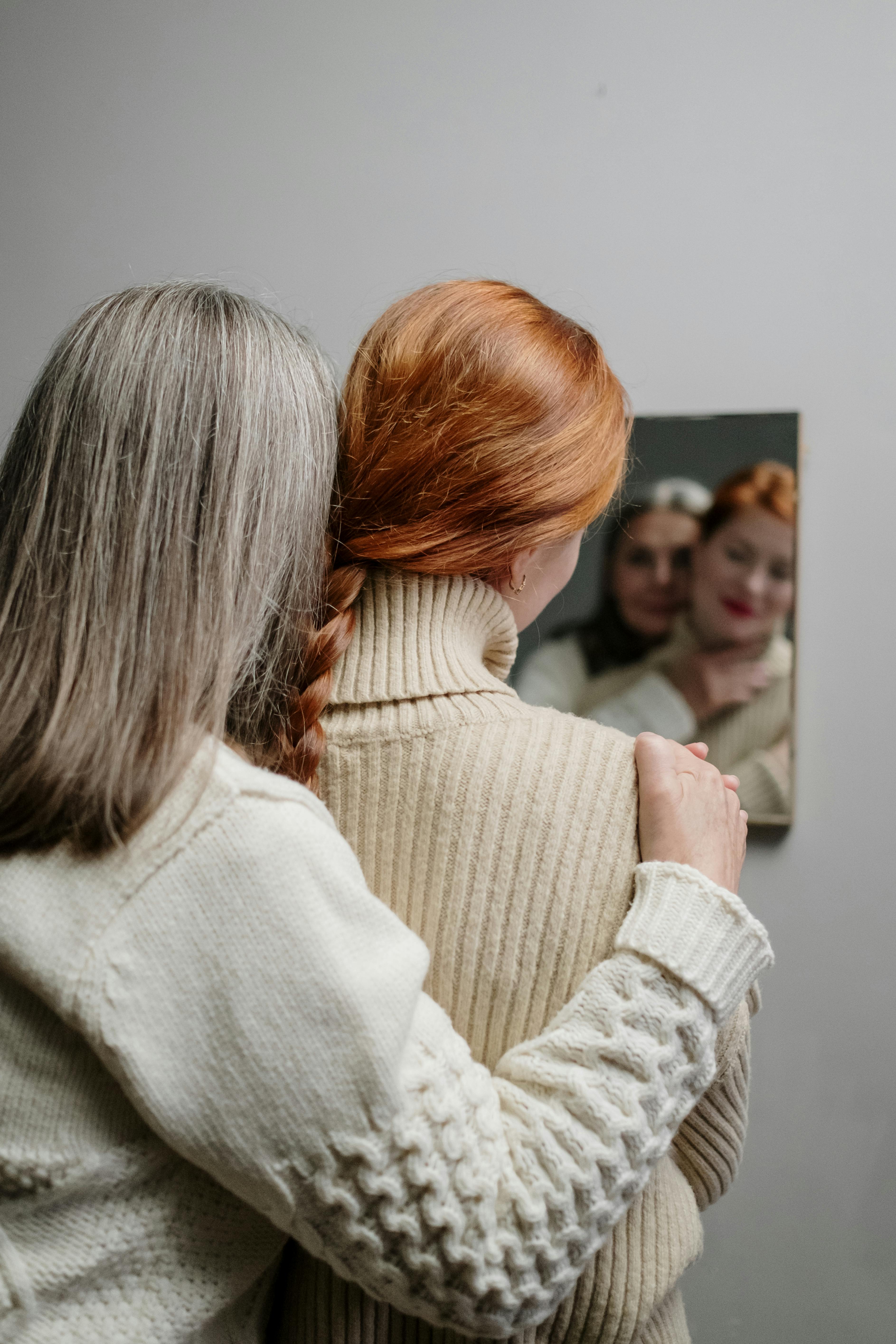 An elderly woman hugs a young woman near a mirror