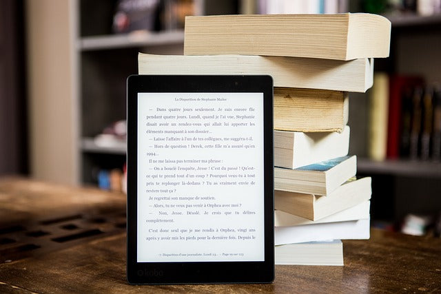 An e-book stands on the table near a stack of books