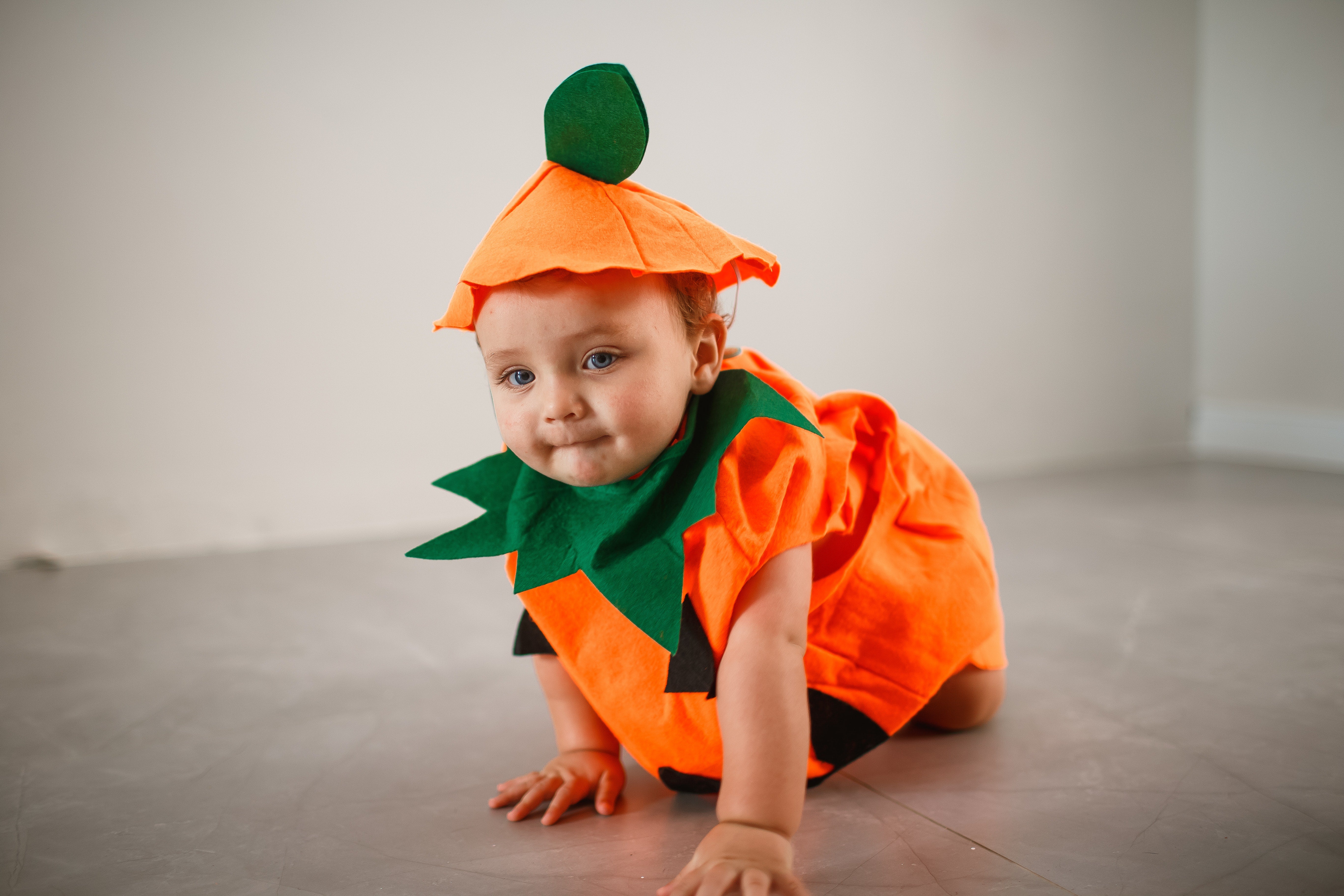 A small child in a pumpkin costume crawls on the floor