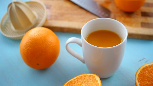 Cup with orange drink, oranges and hand juicer