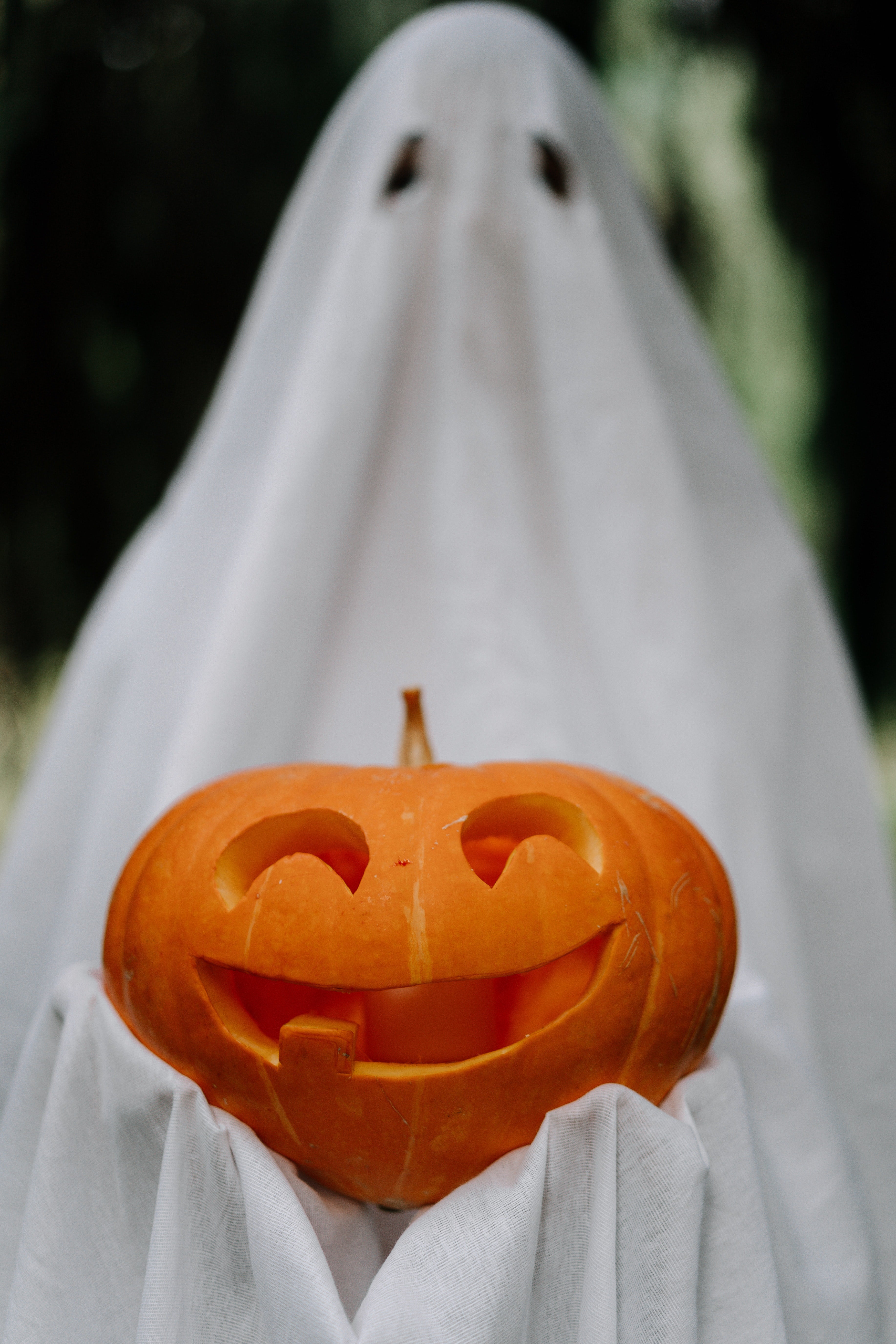 Man in ghost costume holding jack-o'-lantern