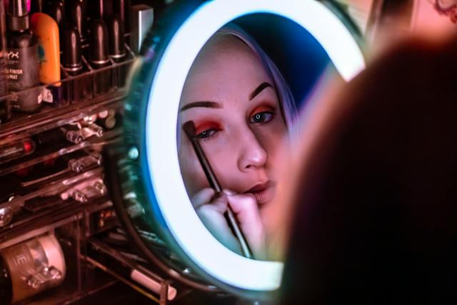 Woman applying makeup to her eyes while looking in a backlit mirror