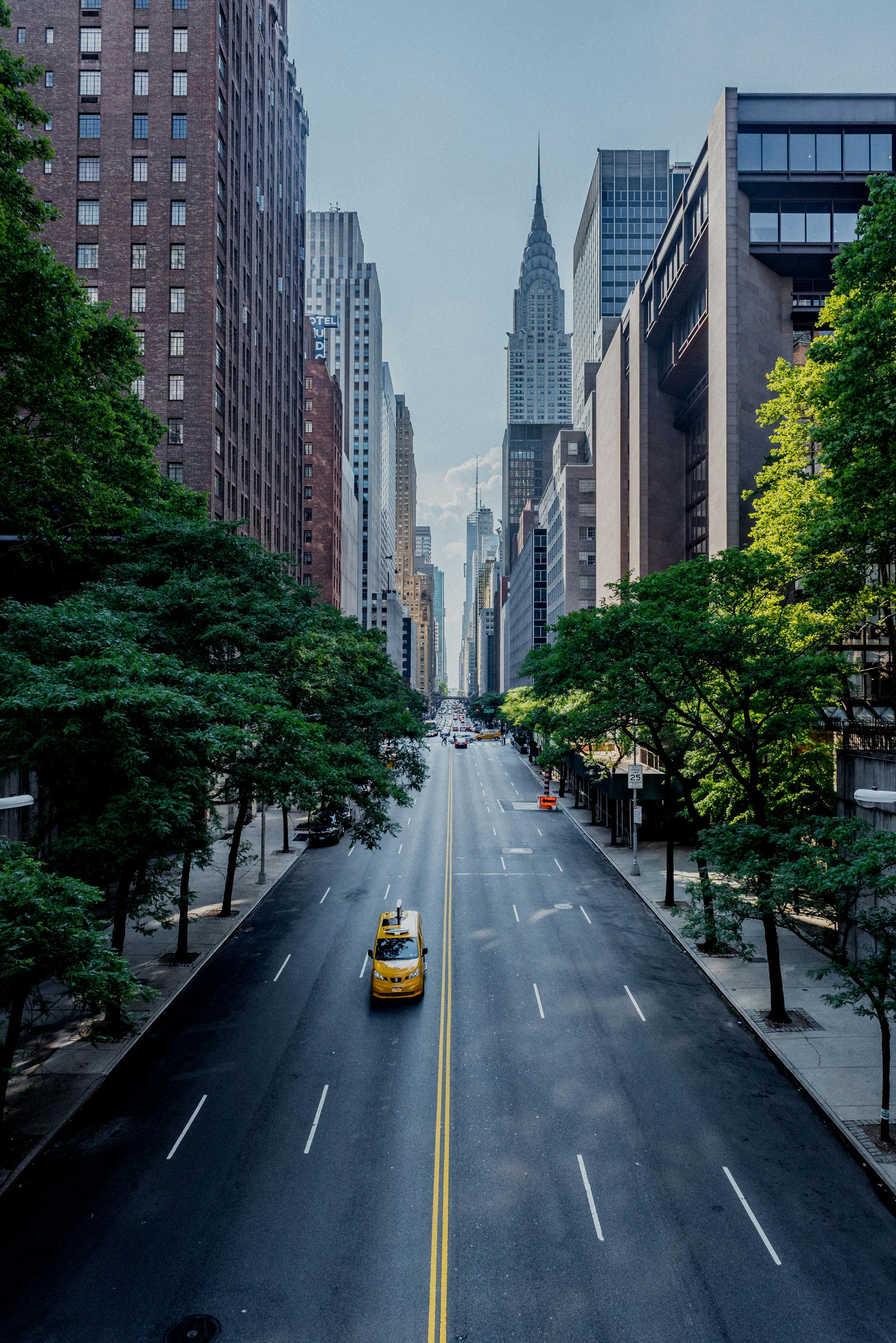 A yellow car drives along the avenue against the backdrop of high-rise buildings