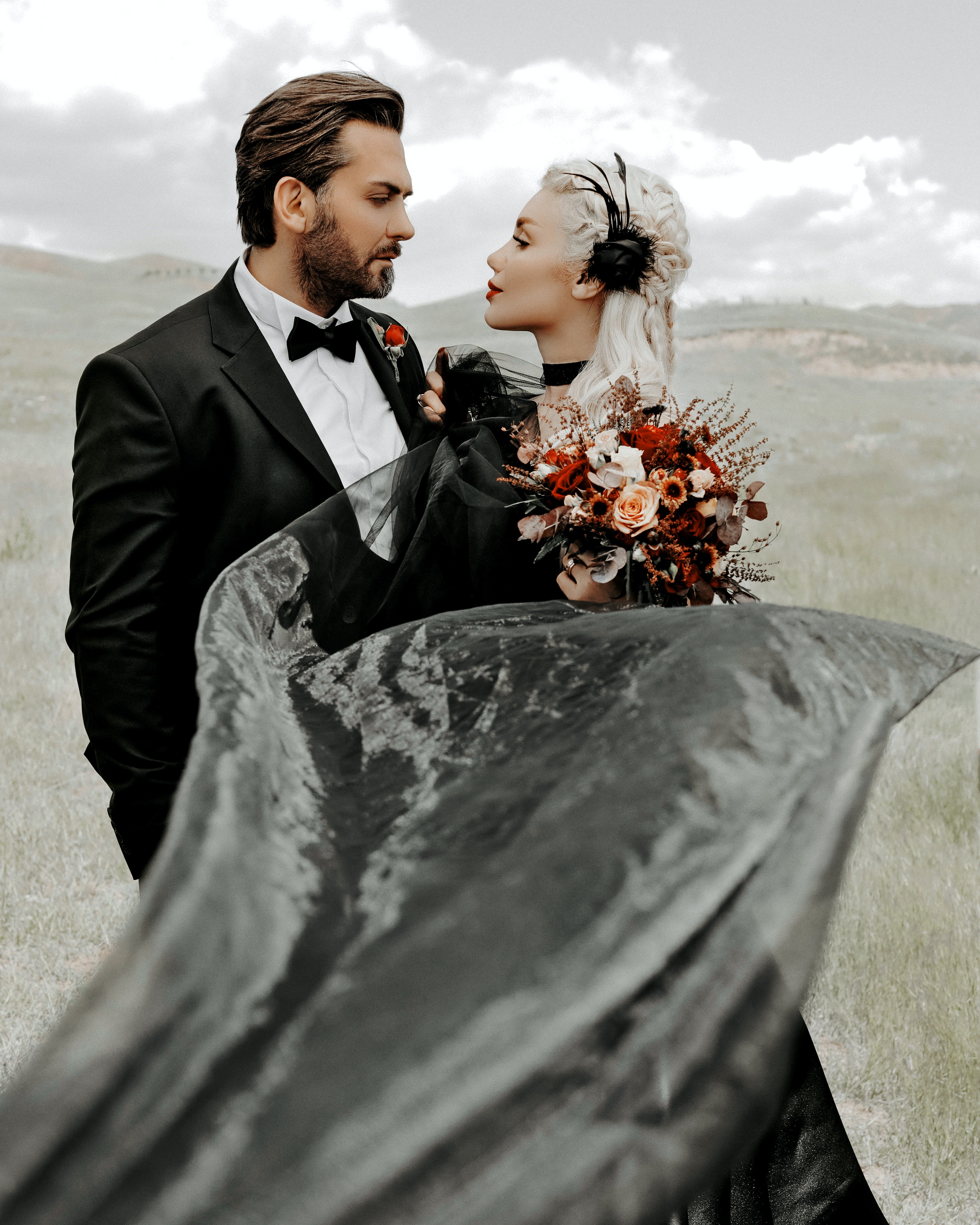 A man in a suit and a woman in a black dress and with a bouquet