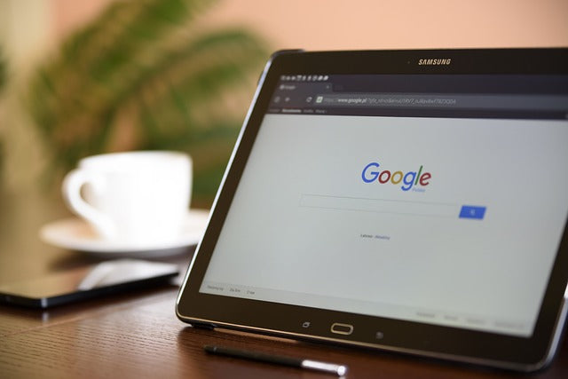 The tablet is on the table, next to it is a smartphone and a white mug.