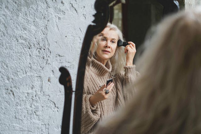 Reflection in the mirror of a woman powdering her temple