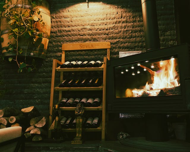 There is a wine cabinet with bottles against the wall next to the fireplace