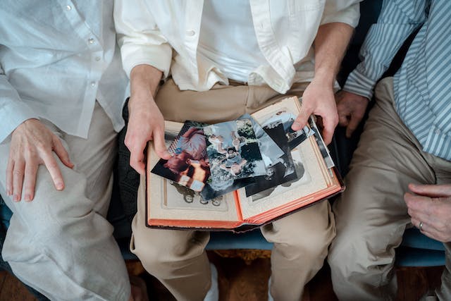 Three people are sitting next to each other, one has an open book and photographs on his lap