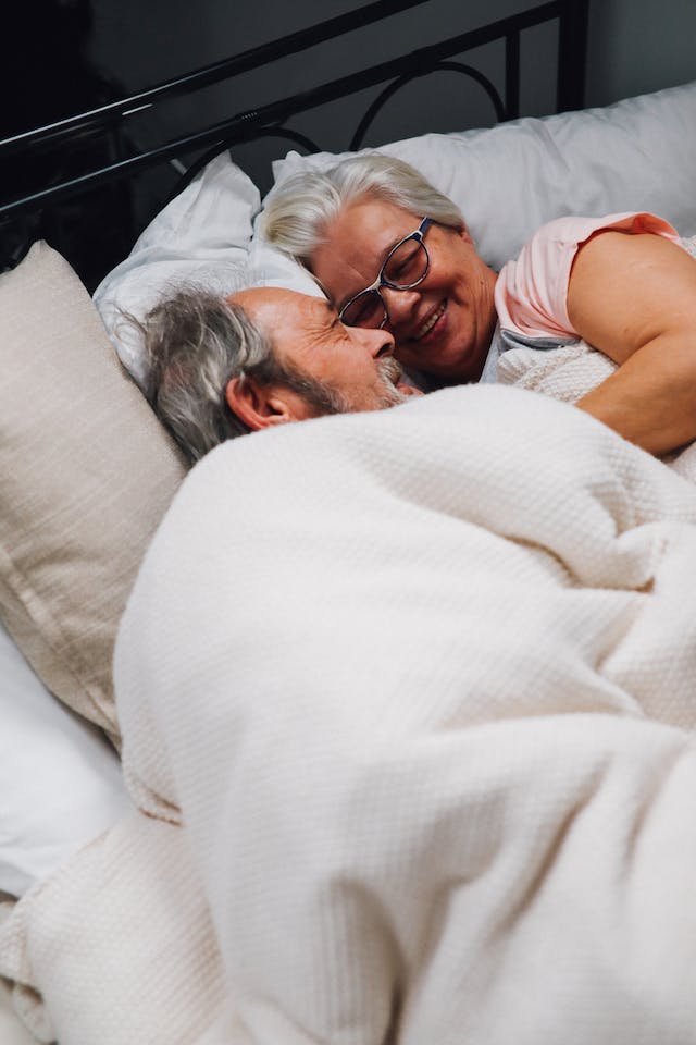 Elderly couple lying on bed under blanket