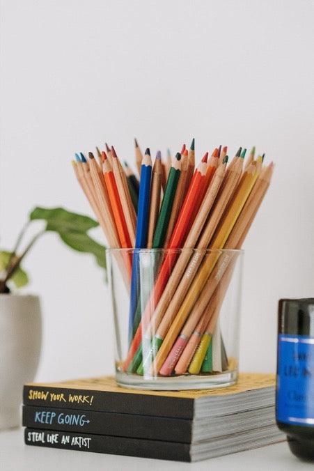 There is a transparent glass on top of a stack of books with colored pencils in it