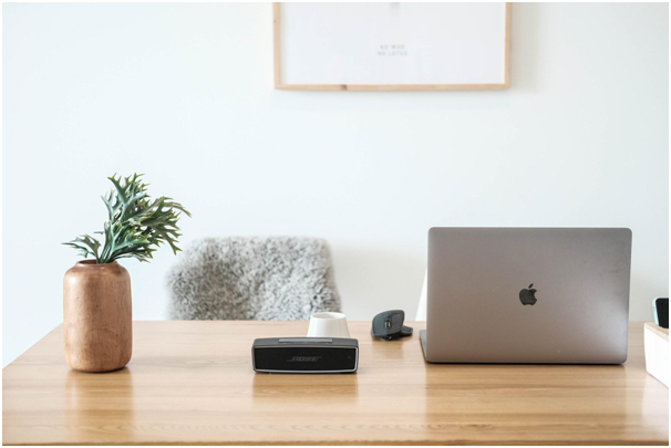 There is a laptop, a vase with a flower and a cup on the office table