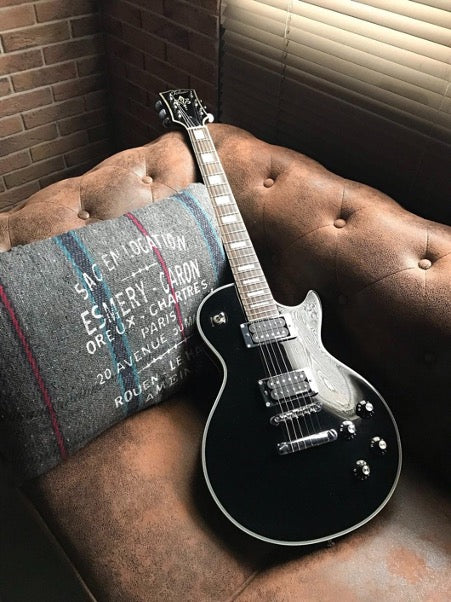  There is a gray pillow and a black guitar on the brown sofa