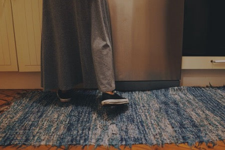 Legs in black shoes and a gray skirt stand on a white and blue rug