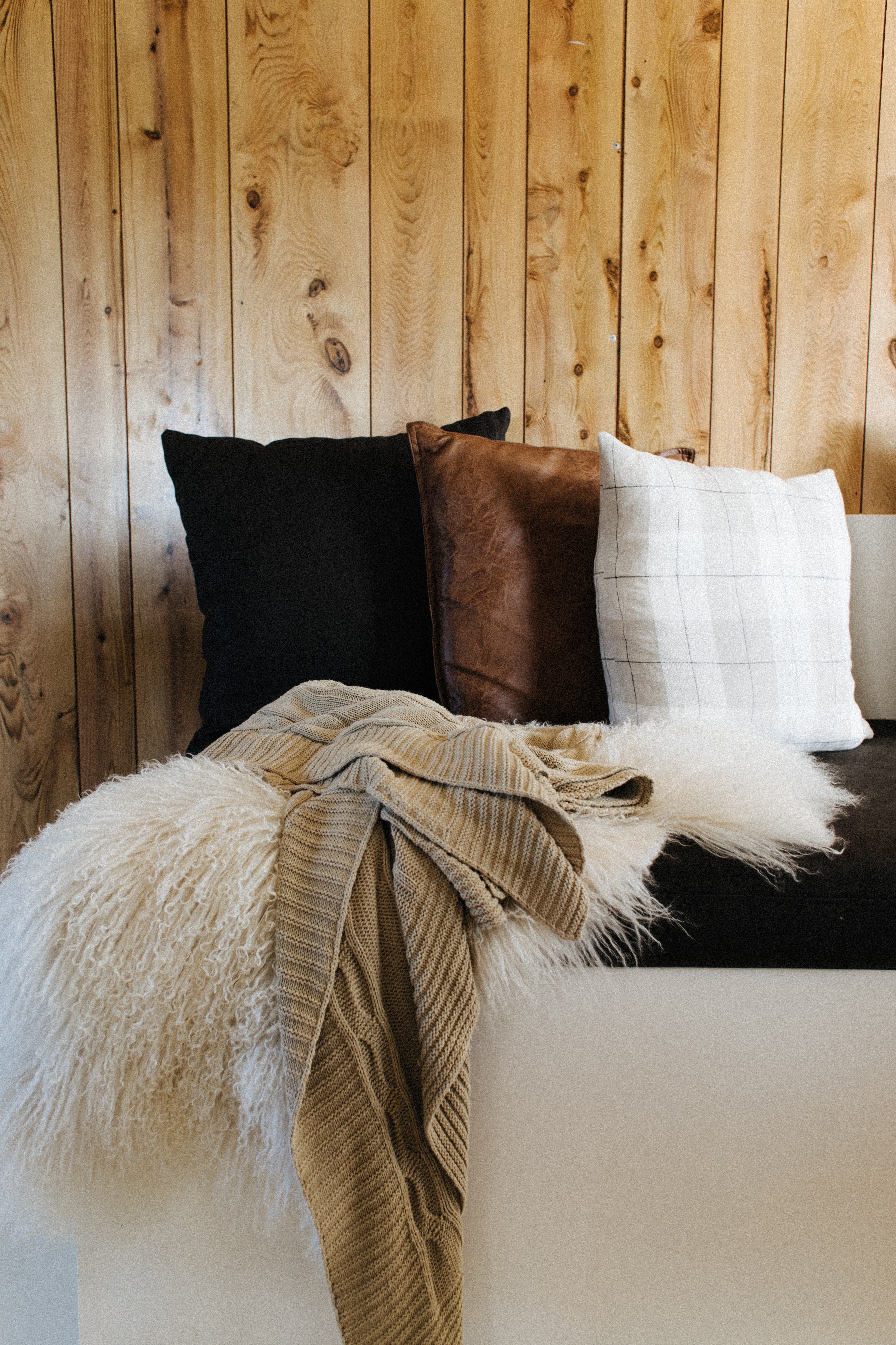 Three pillows on a bed near a wooden wall