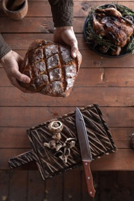 There are a cutting board and a knife on the table, and above the table, hands holds bread