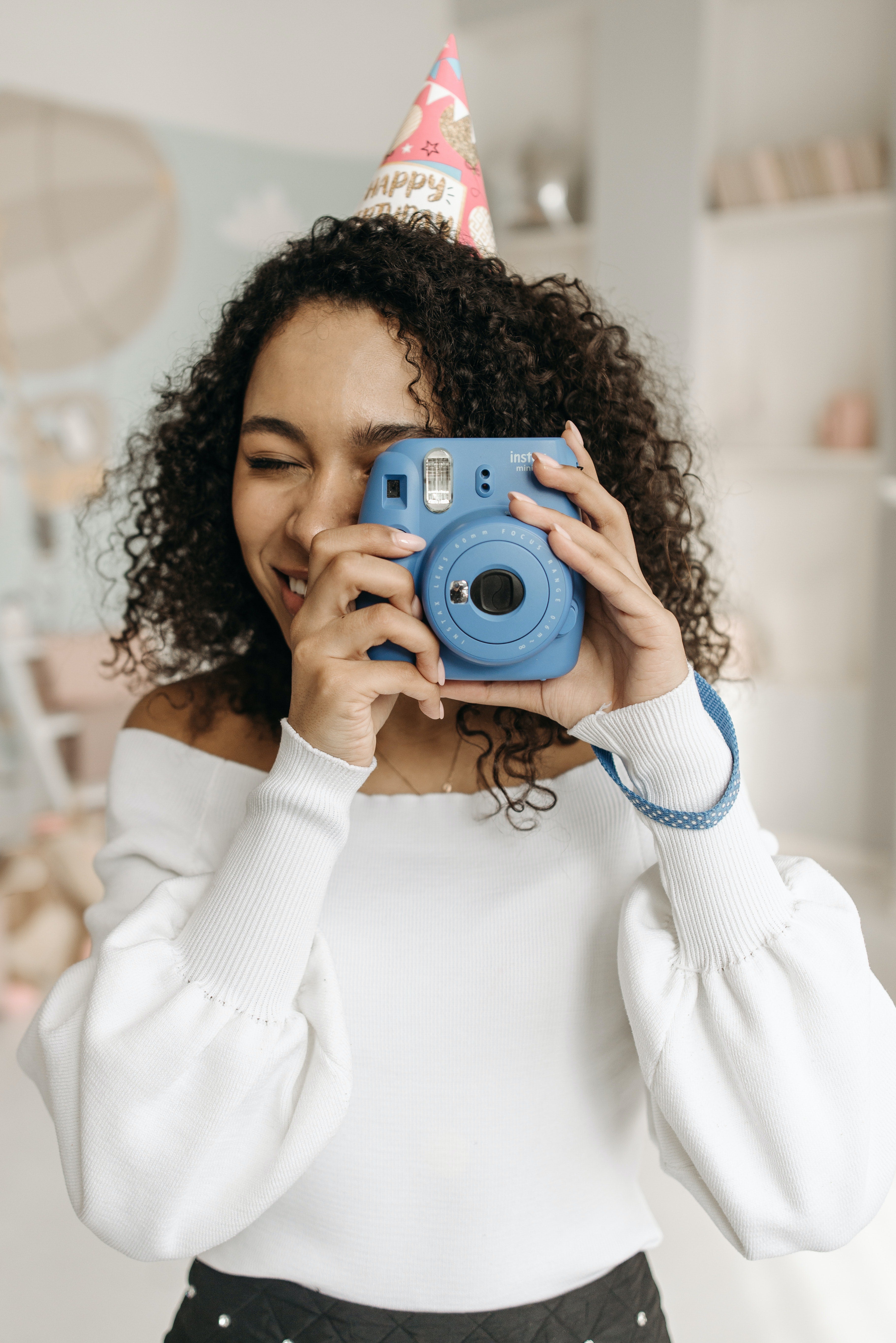 A woman in a white sweater holds a blue polaroid in front of her face