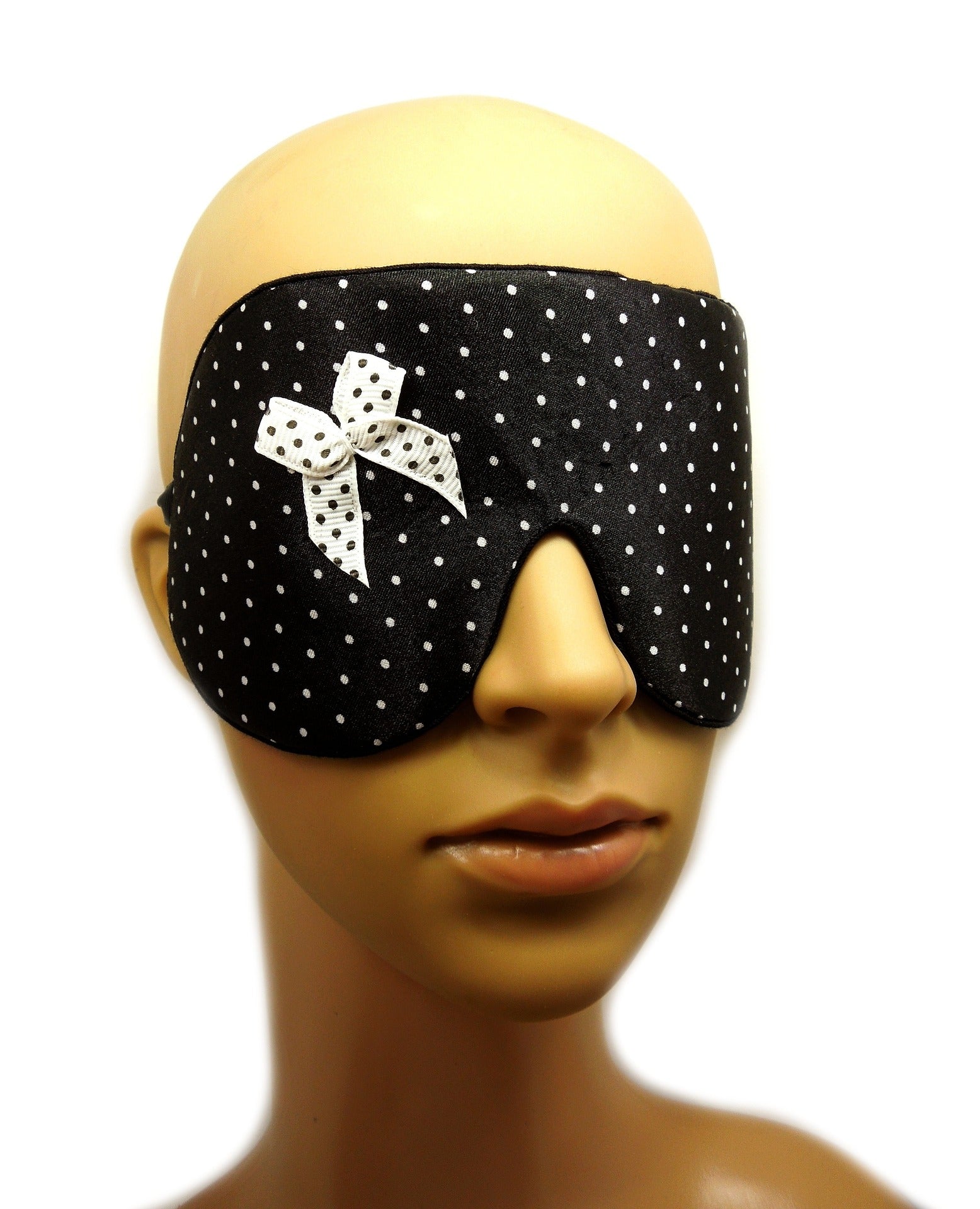  A black polka dot sleep mask with a bow is worn on a mannequin