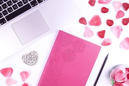 A pink notepad and a pencil lie on the table next to a laptop