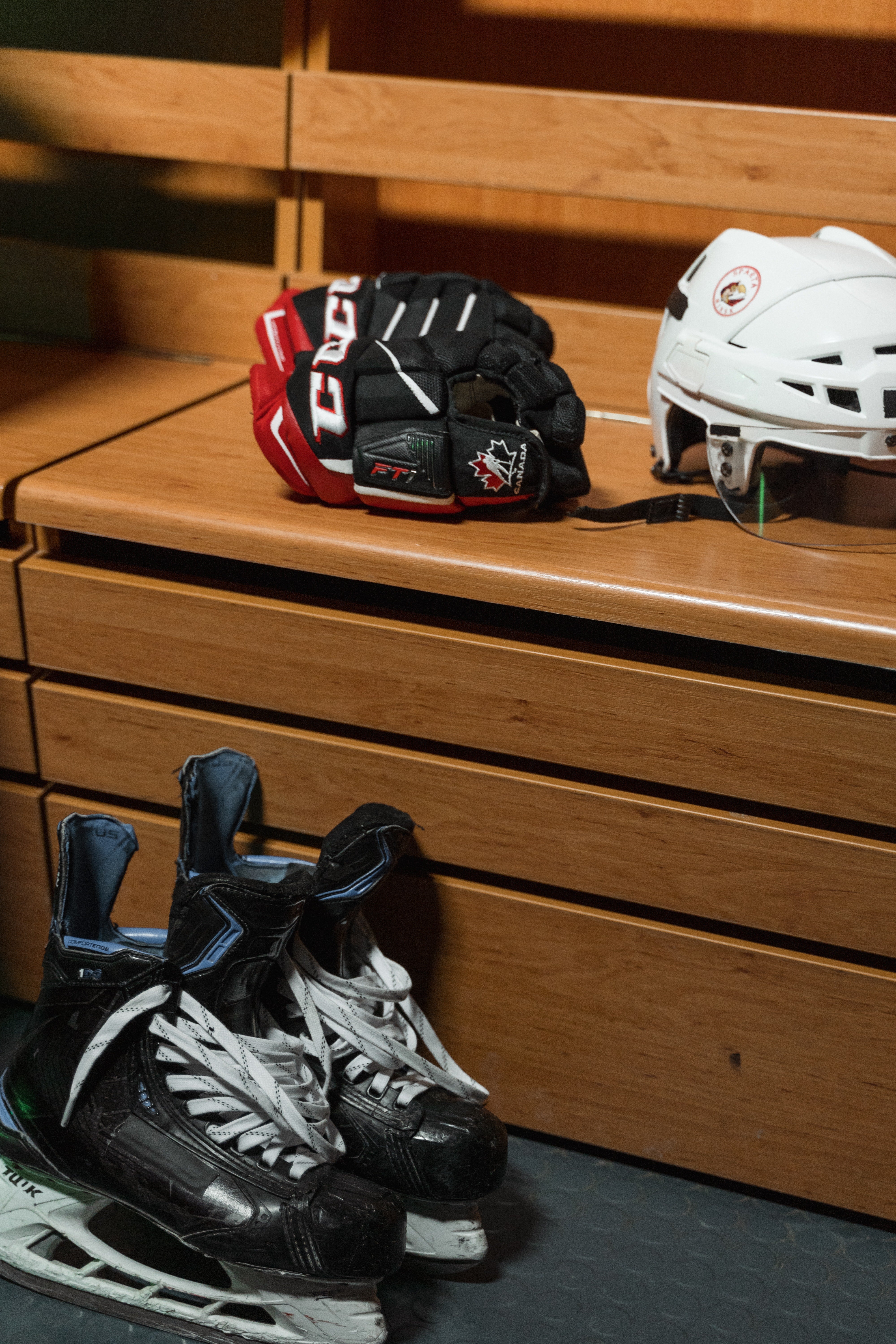 Hockey helmets lie on a wooden bench, and hockey skates stand nearby