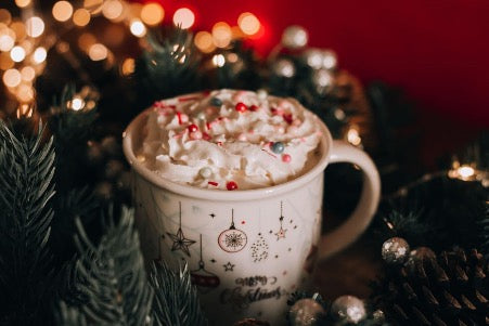 White mug with milk foam and decorations surrounded by fir branches