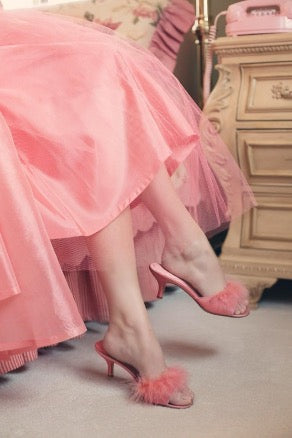 Legs of a woman wearing a pink dress and pink shoes with a fluffy top