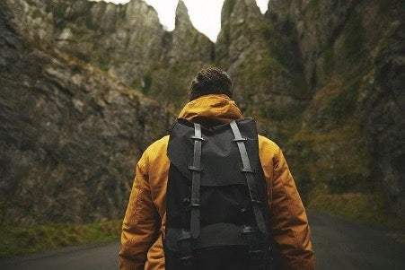 A man in a yellow jacket and with a black backpack on a background of mountains