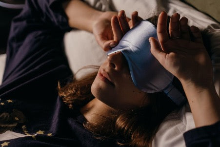 Woman in relaxing eye mask and black pajamas lies on the bed