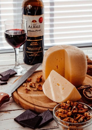 There is a wooden board with cheese, a plate with walnuts and a bottle of wine and a glass on the table