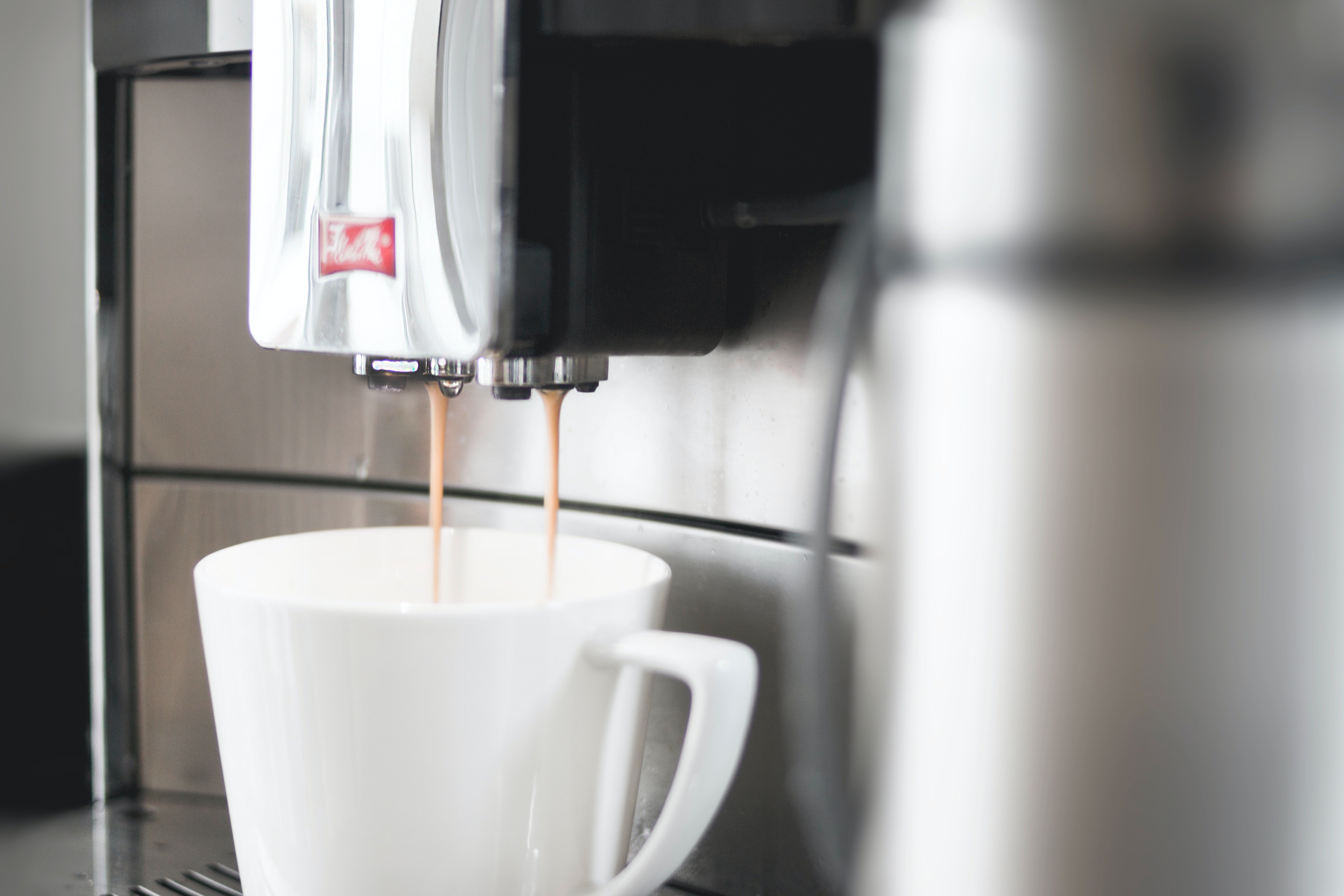 Coffee is pouring from a coffee machine into a white mug