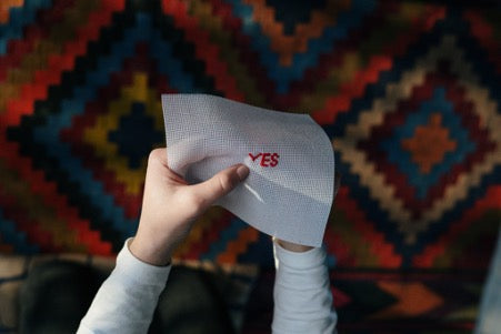 Hands holding a white cloth with the word yes embroidered in red