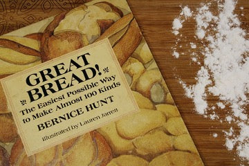 The recipe book is on the brown table next to the scattered flour