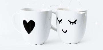  Two white cups, one with a heart print, the other with closed eyes and a smile