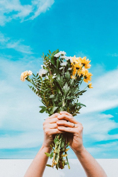 Hands hold a bouquet of flowers against the sky