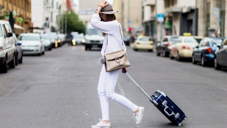 Woman in white clothes with a black suitcase crosses the road