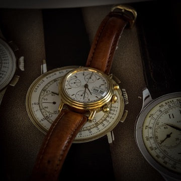 A wrist watch with a brown strap lies on the dial of a larger watch