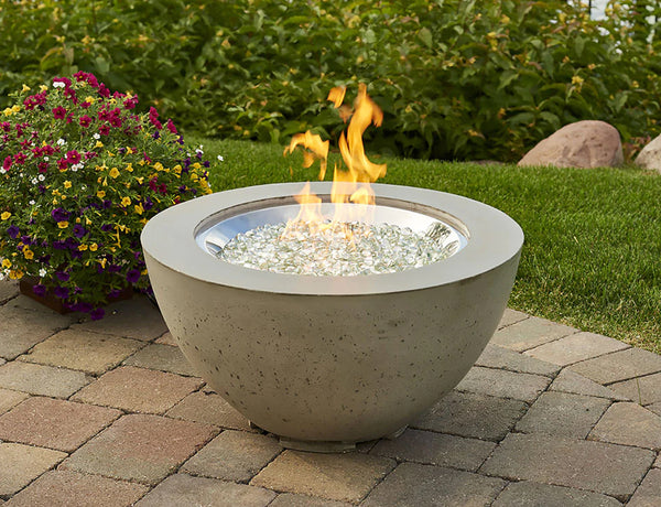 A gas firebowl on a patio with greenery in the background.
