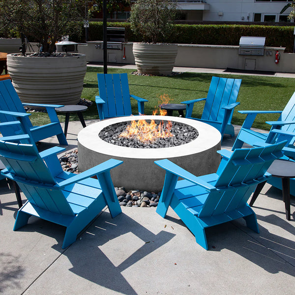 A Rotondo 80 Outdoor Fire Pit with blue adirondack chairs around it.