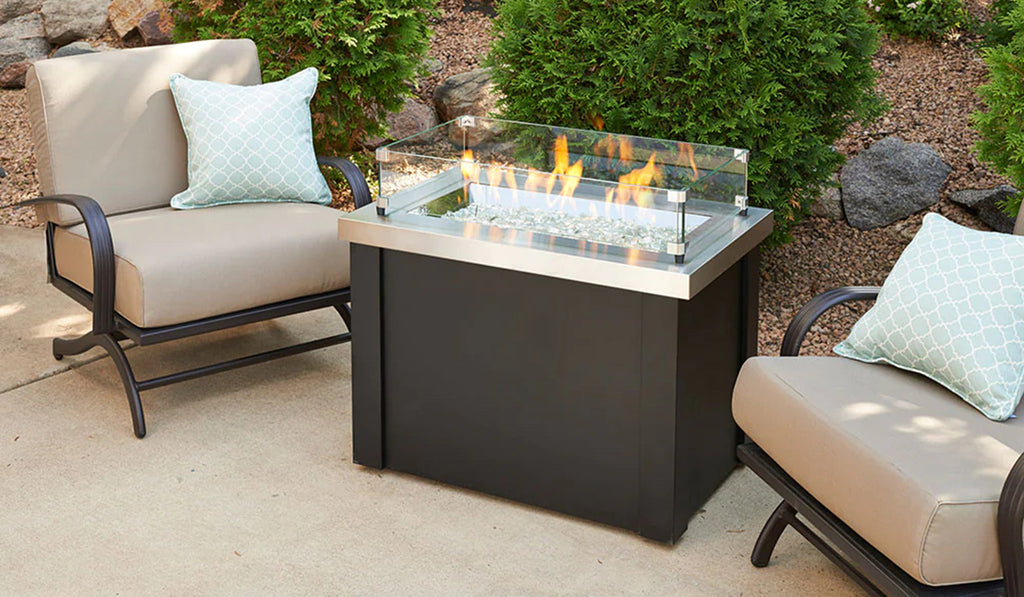 Tabletop firepit on a patio with glass sides and beige lounge chairs.