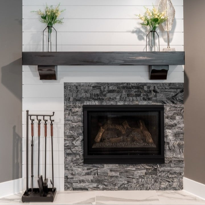 Stacked stone fireplace surround with wood mantel and fireplace tools.