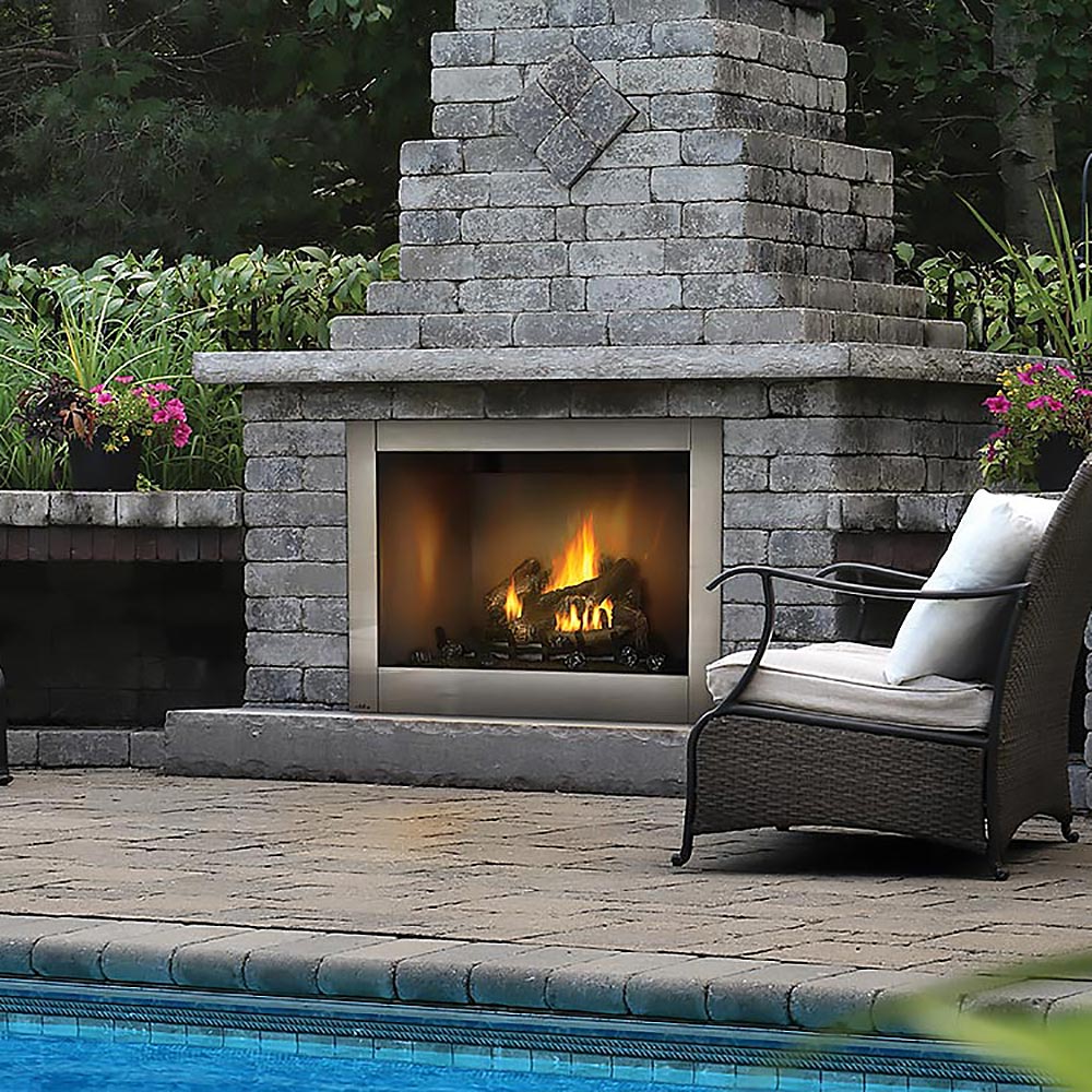 Stacked stone fireplace beside a pool with patio furniture.