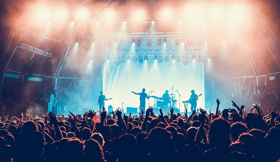 Band playing at concert with lights on and crowd cheering.