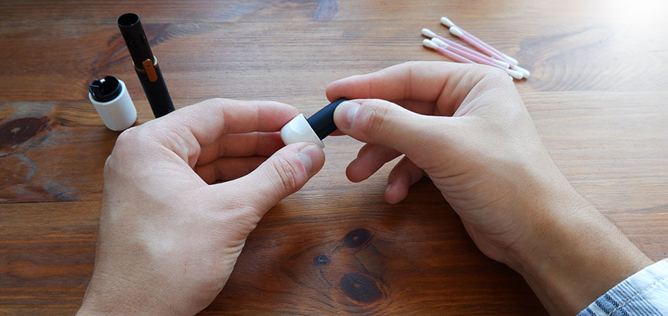 Electronic e-cigarette in mans hand with cleaning swabs to one side and components on the table.